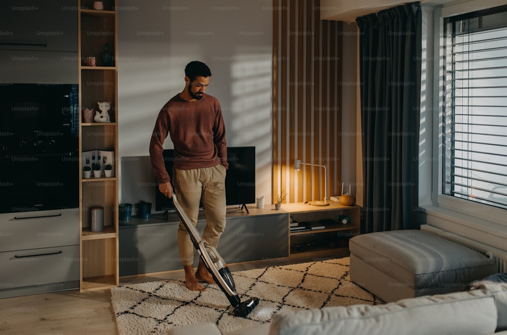 Ein junger Mann saugt Teppich im Wohnzimmer