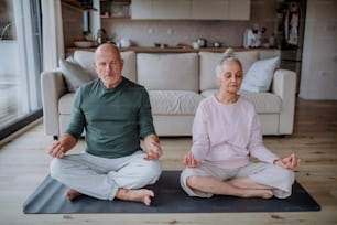 A senior couple doing relaxation exercise together at home.