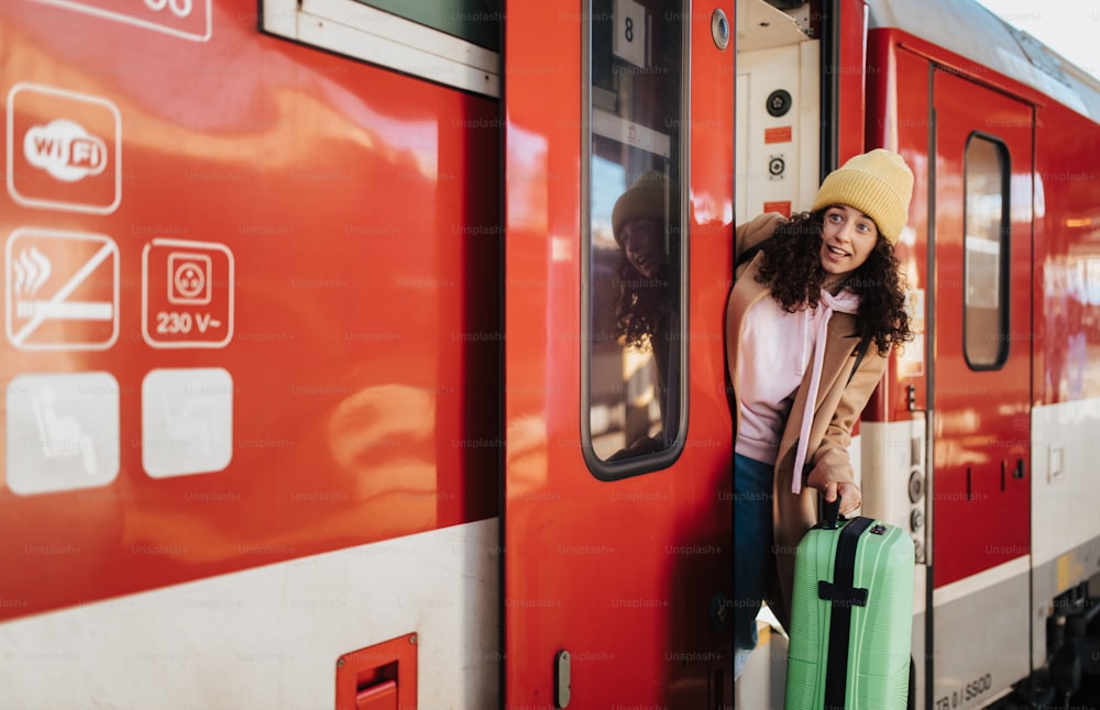 Eine glückliche junge Reisende mit Gepäck steigt am Bahnsteig aus