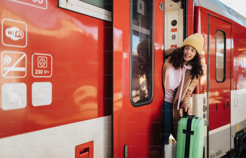 Una giovane donna viaggiatrice felice con i bagagli che scende dal treno alla piattaforma della stazione ferroviaria