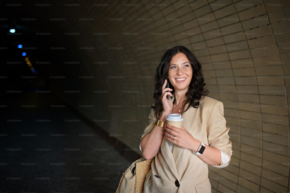 A successful happy businesswoman commuting in the morning in city street, calling on mobile phone and holding cofee cup.