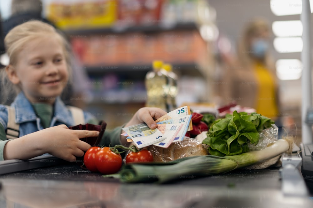 Gros plan d’une petite fille blonde qui paie ses courses au supermarché.
