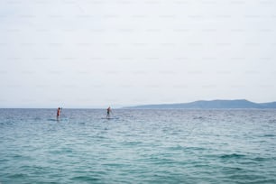 Uomini che trascorrono il tempo libero mentre si divertono a pagaiare su un SUP in mare durante l'estate. Concetto di vacanza estiva.