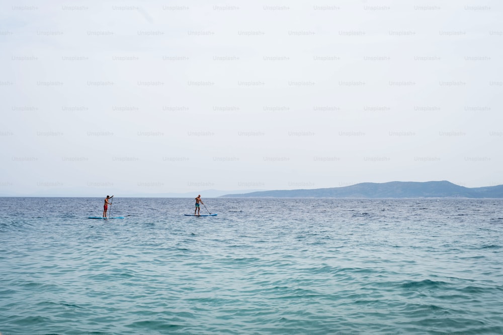 Hombres que pasan el tiempo libre mientras disfrutan remando en un SUP en el mar durante el verano. Concepto de vacaciones de verano.