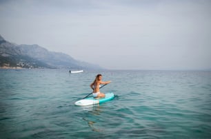 Uma jovem mulher bonita em um biquíni em uma prancha de SUP no mar. Garota de aventura em Standup paddleboarding com um remo no oceano. Vista traseira.