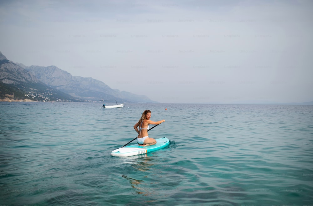 Eine junge schöne Frau im Bikini auf einem SUP-Board im Meer. Abenteuermädchen auf Standup-Paddleboarding mit einem Paddel im Meer. Rückansicht.