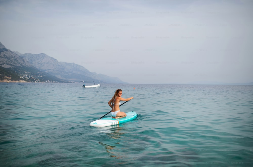 Una giovane bella donna in bikini su una tavola da SUP in mare. Ragazza avventurosa su Standup paddleboarding con una pagaia nell'oceano. Vista posteriore.
