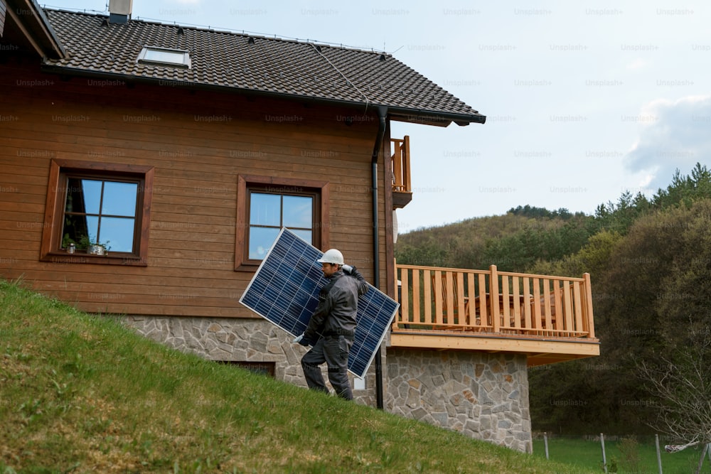 Un trabajador que lleva un panel solar para instalar un sistema de módulo solar en la casa.