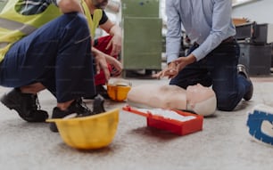 Ein männlicher Ausbilder zeigt erste medizinische Hilfe an der Puppe während des Trainingskurses in Innenräumen