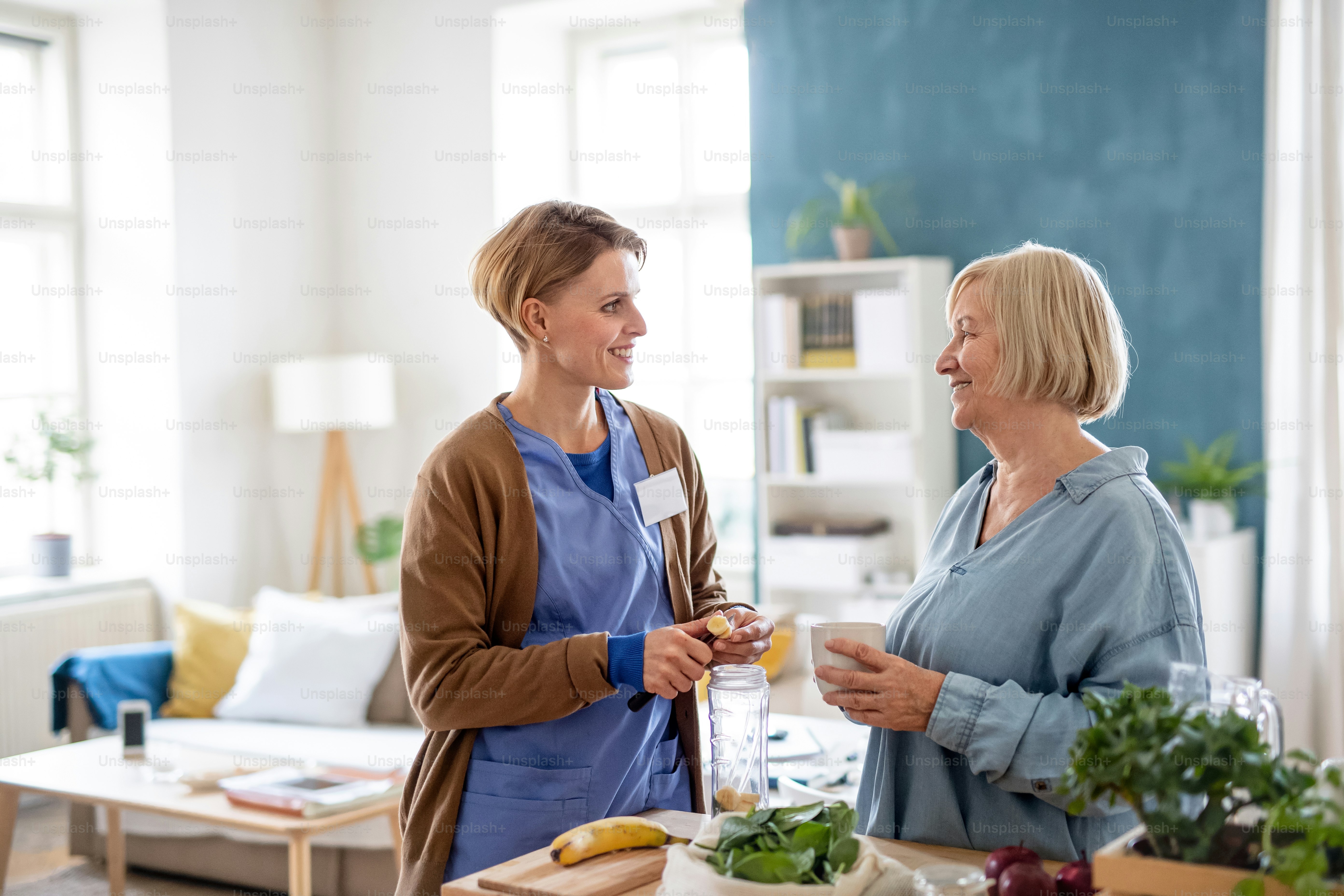 Happy senior woman with caregiver or healthcare worker indoors, preparing food