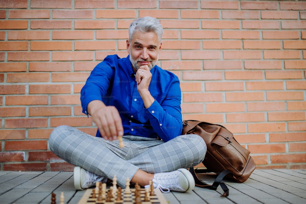 A successful happy businessman sitting in city street and playing chess.