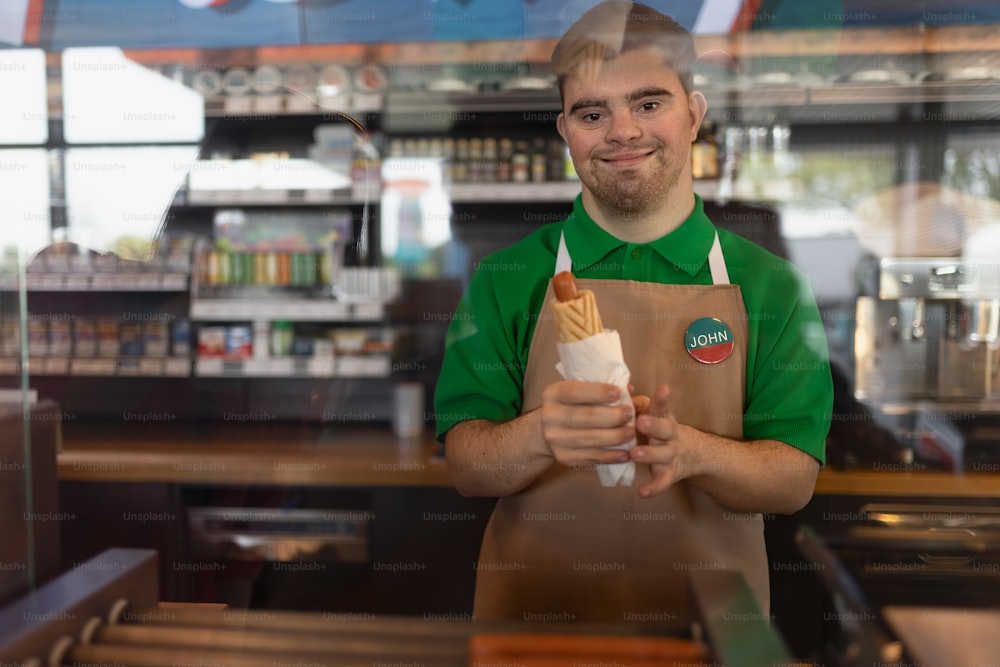 Un camarero feliz con síndrome de Down sirviendo baguette y pasándosela al cliente en la cafetería de la gasolinera.