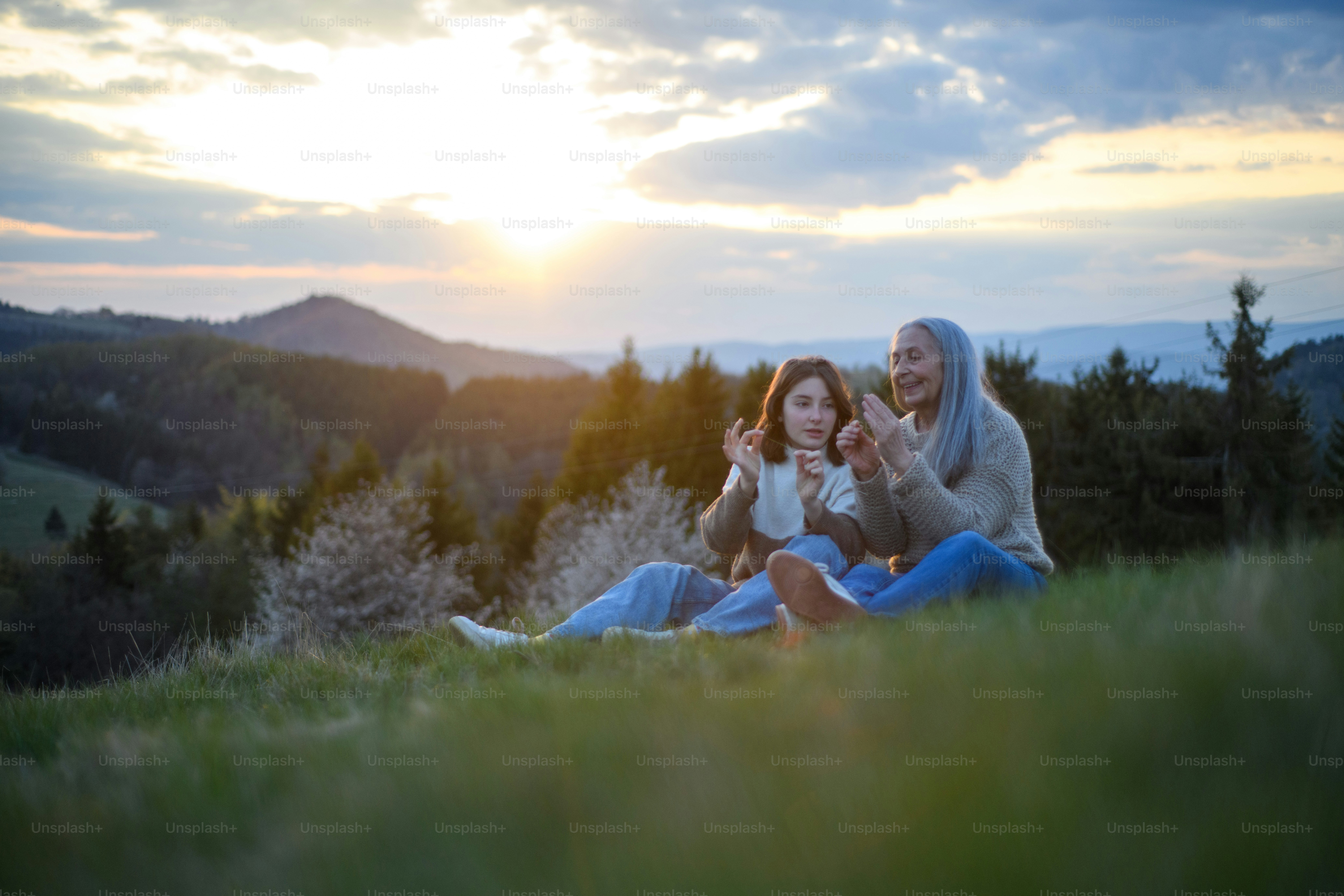 Une grand-mère âgée heureuse avec un grand-père adolescent assis et sifflant sur l’herbe dans la nature un jour de printemps.