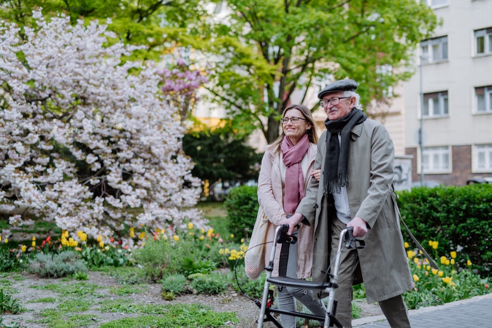 Un uomo anziano con deambulatore e figlia adulta all'aperto su una passeggiata nel parco.