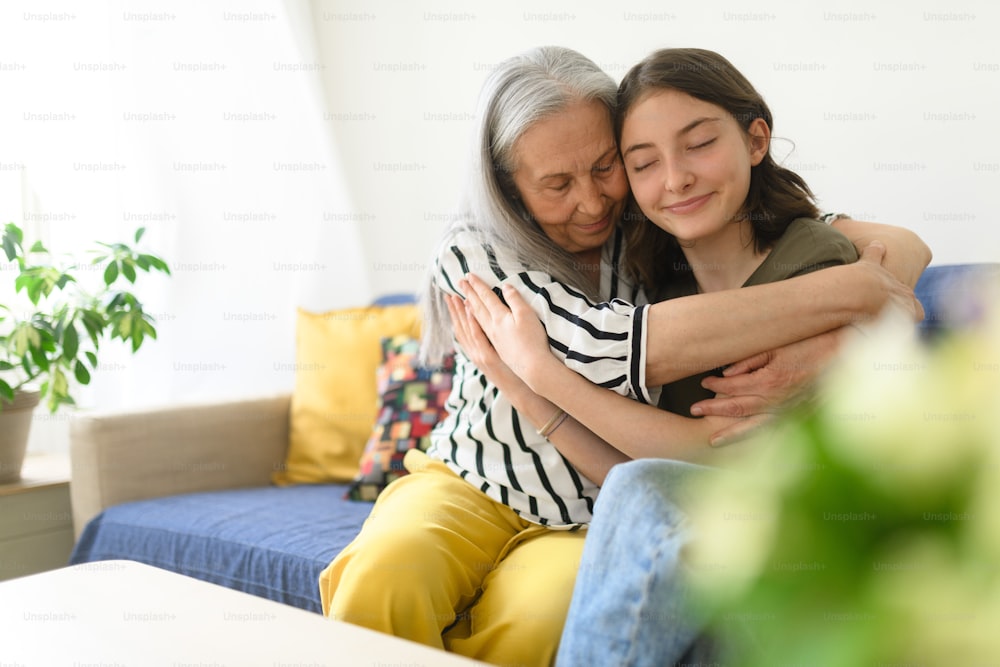 A senior grandmother with teenage granddaguhter having good time together at home, hugging.