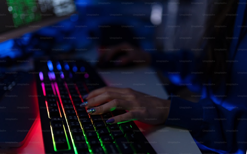 Primo piano di una donna hacker mani al computer tastiera nella stanza buia di notte, concetto di guerra cibernetica. Vista laterale.