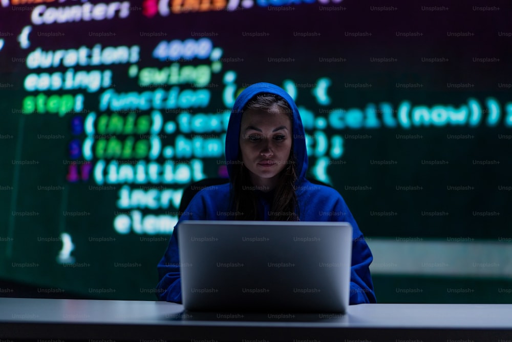 밤에 어두운 방에서 컴퓨터로 두건을 쓴 익명의 해커 여성, 사이버 전쟁 개념.