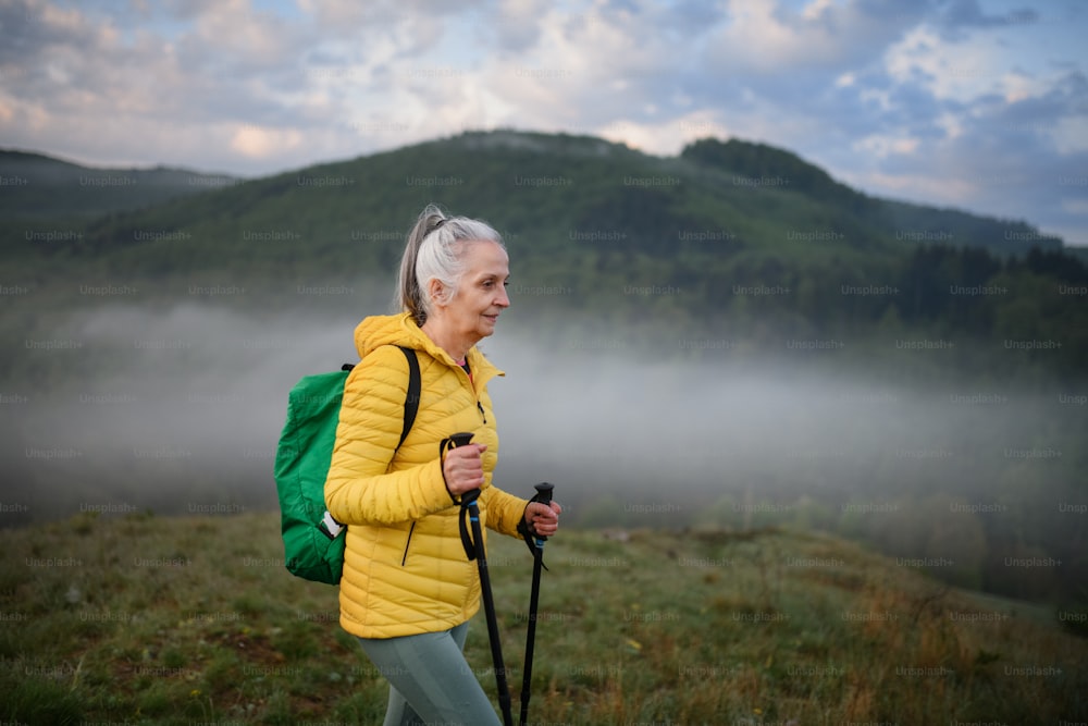 Una mujer mayor caminando en la naturaleza temprano en la mañana con niebla y montañas en el fondo.