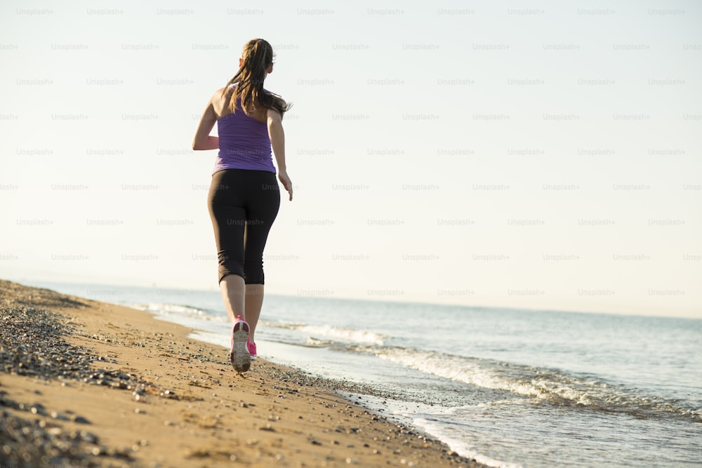 La giovane donna sta correndo nella natura soleggiata lungo la spiaggia