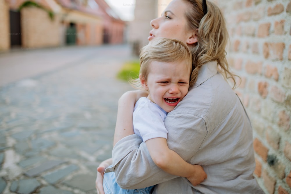 Uma mãe constrangendo sua filhinha chorando, segurando-a nos braços na rua no verão.