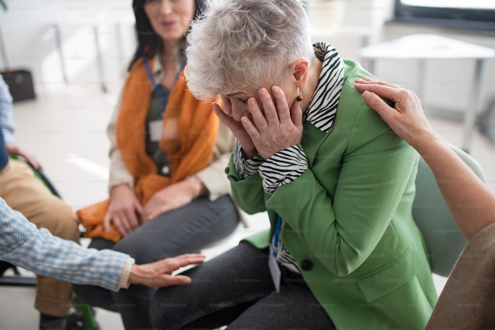 Um grupo de pessoas idosas sentadas em círculo durante a sessão de terapia, consolando a mulher deprimida.