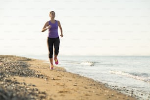 Jeune femme court dans la nature ensoleillée le long de la plage