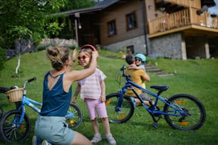 A young family with little children preaparing for bike ride, putting on helmets in front of house.