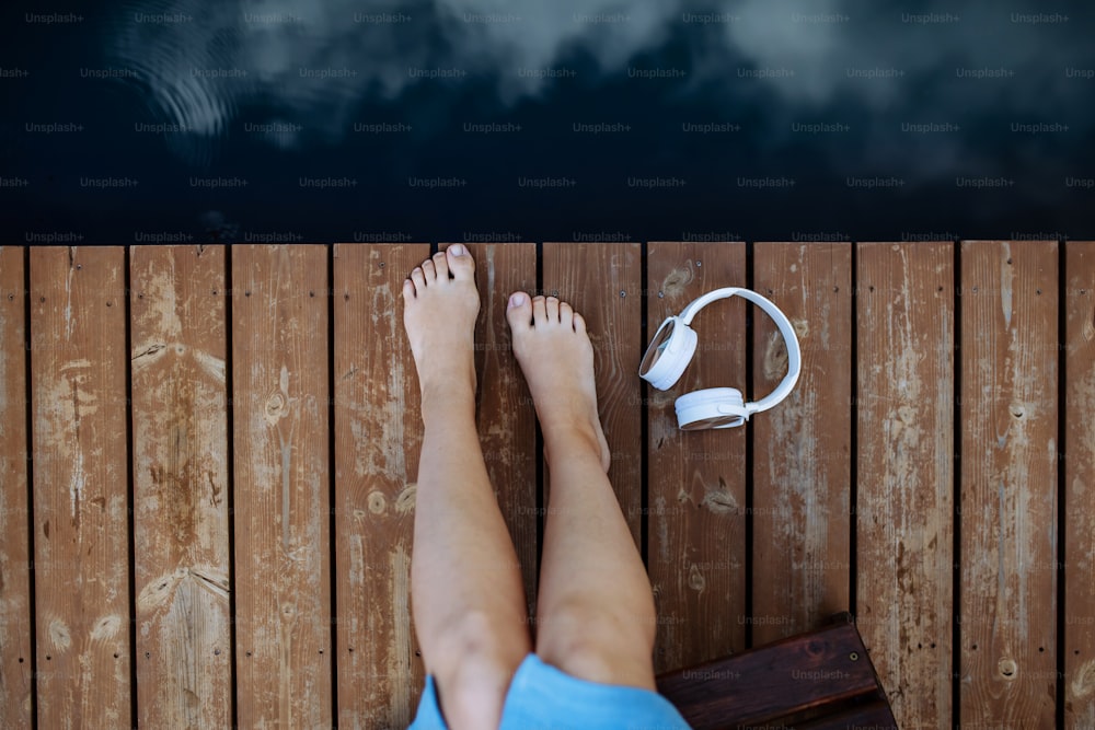 Close-up of womans legs and a headphones lying on a pier by natureal lake in summer Top view.