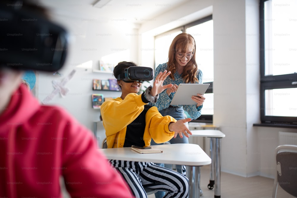 Young high school teacher giving lesson to students with VR goggles in a classroom