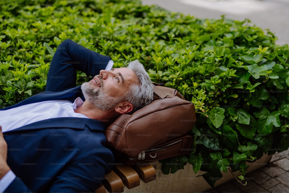 Un homme d’affaires mature se détendant sur un banc dans un parc de la ville pendant une pause au travail, concept d’équilibre entre vie professionnelle et vie privée.