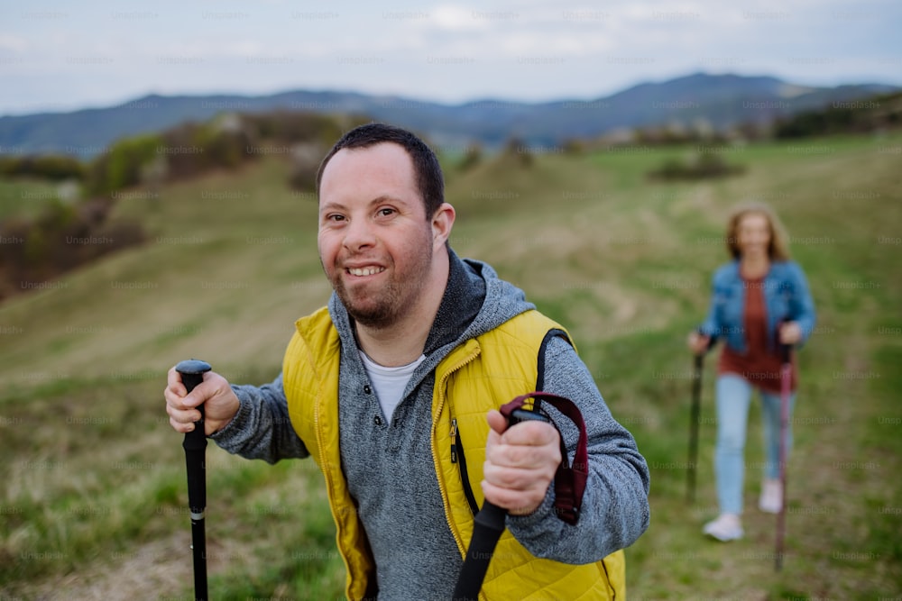 A portrait of happy young man with Down syndrome with his mother hiking together in nature.
