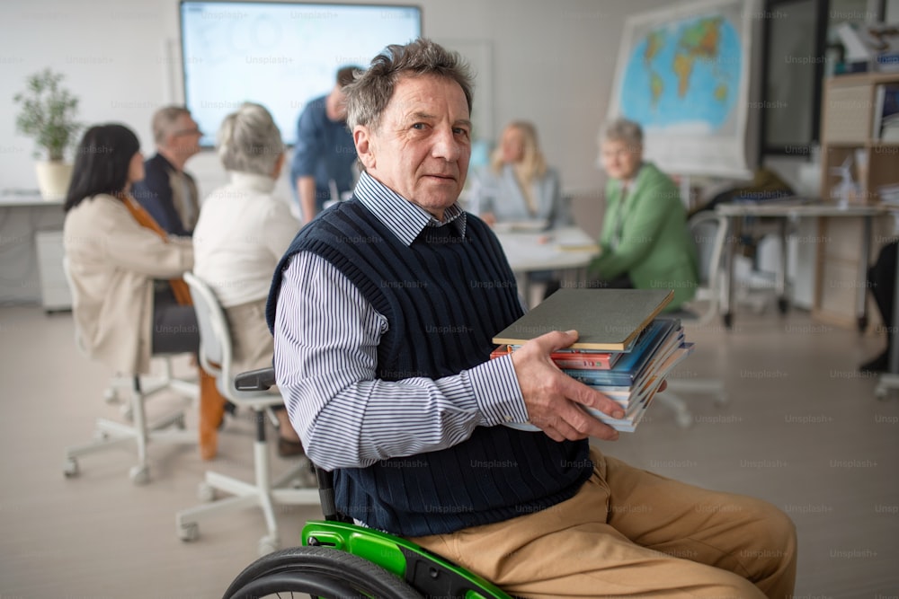 A happy disabled man senior student on wheelchair holding books and looking at camera during class at university.