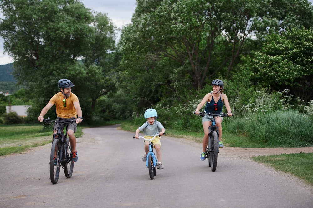 A young family with little child riding bicycles on road in village in summer.