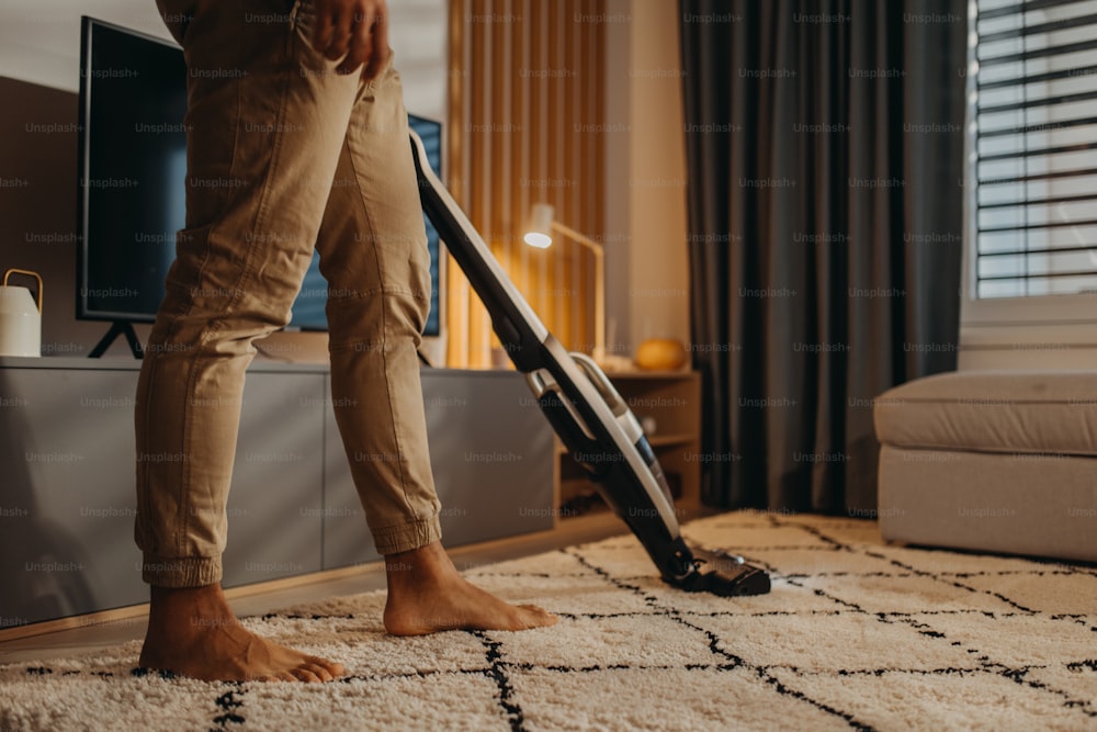 A lowsection of man hoovering carpet with vacuum cleaner in living room