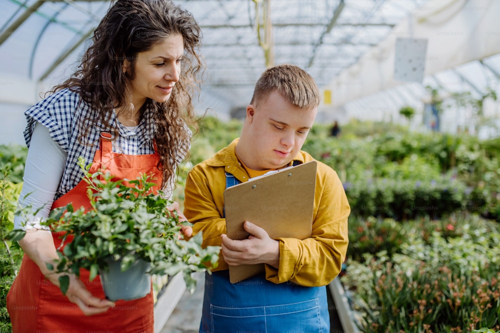 Una florista experimentada ayuda a un joven empleado con síndrome de Down a revisar las flores en una tableta en un centro de jardinería.