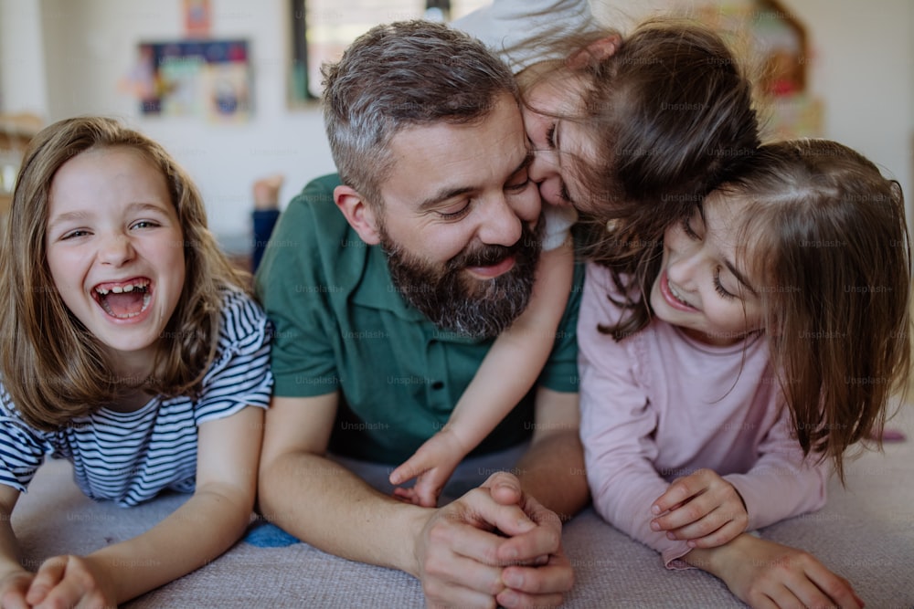 Um pai alegre com três filhas pequenas brincando juntas em casa.