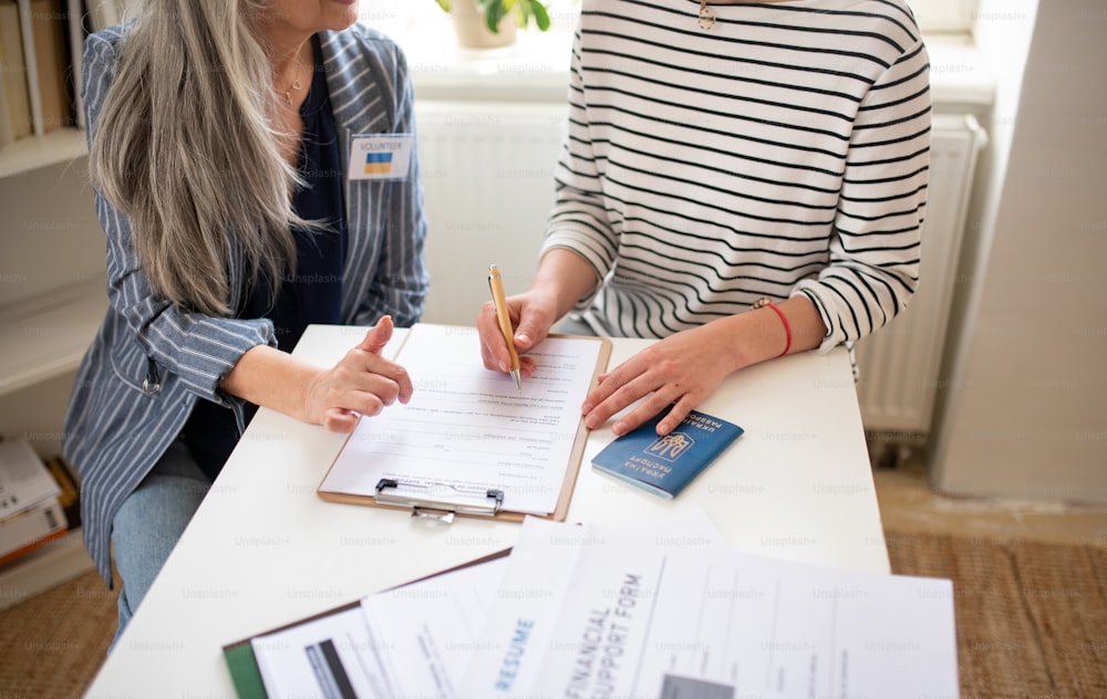 A senior woman volunteer helping Ukrainian woman to fill in forms at asylum centre.