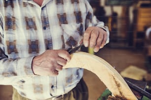 Senior craftsman working with planer on wooden pole in his workshop