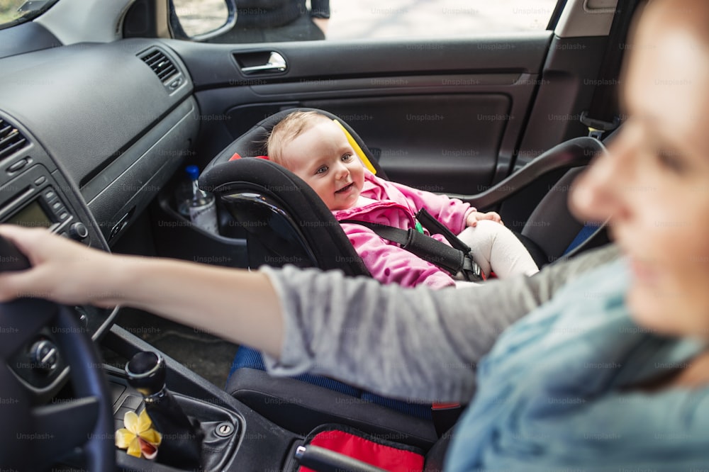 Mother driving a car, having her little baby girl in a child seat