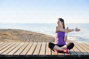Young woman is doing exercises on pier close to the beach