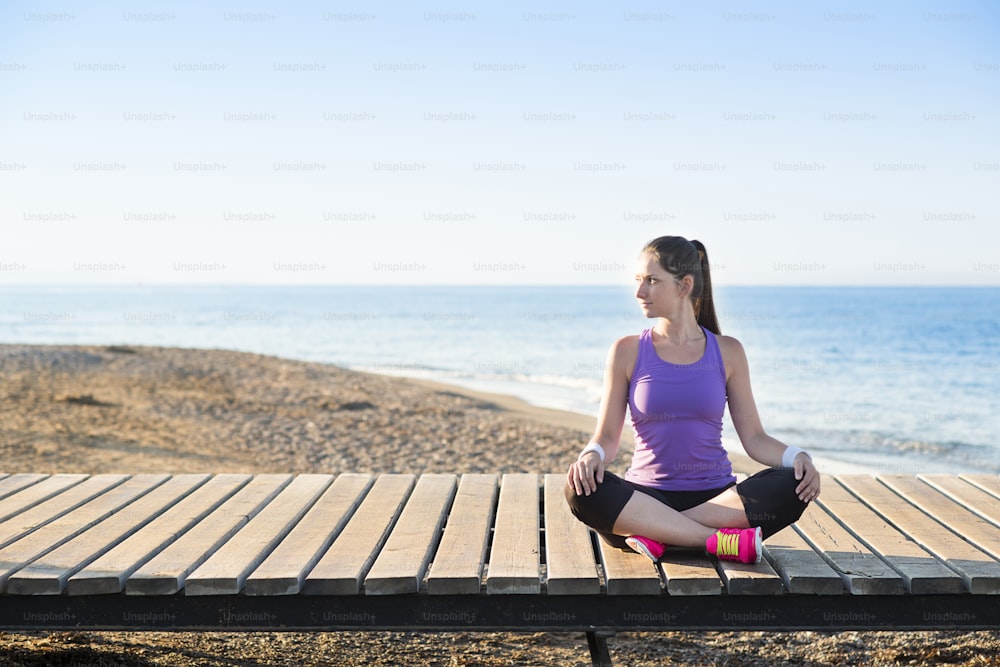 Young woman is doing exercises on pier close to the beach