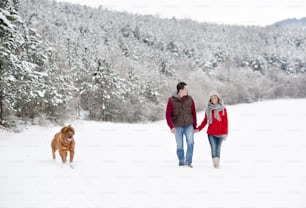 Une femme et un homme se promènent avec un chien dans la campagne enneigée d’hiver
