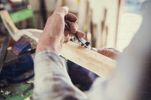 Leitender Handwerker arbeitet mit Hobel an Holzstangen in seiner Werkstatt