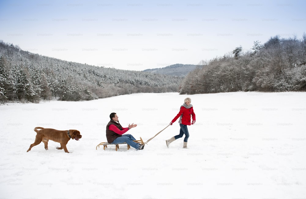 Woman and man are having walk with dog in winter snowy countryside