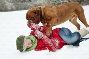 ブロンドの女の子は雪の中で彼女の大きな茶色の犬と楽しんでいます