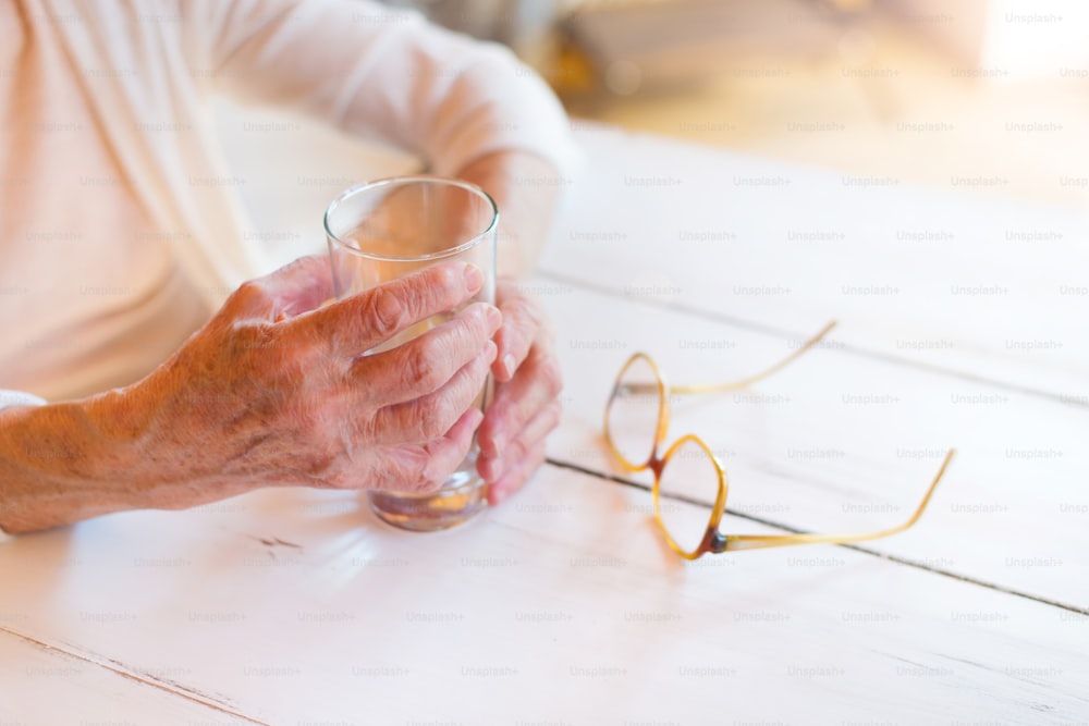 Hands of unrecognizable senior woman holding a glass of water