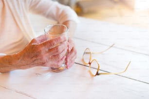 물 한 잔을 들고 있는 알아볼 수 없는 노인 여성의 손