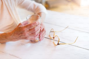 Mani di donna anziana irriconoscibile che tiene un bicchiere d'acqua