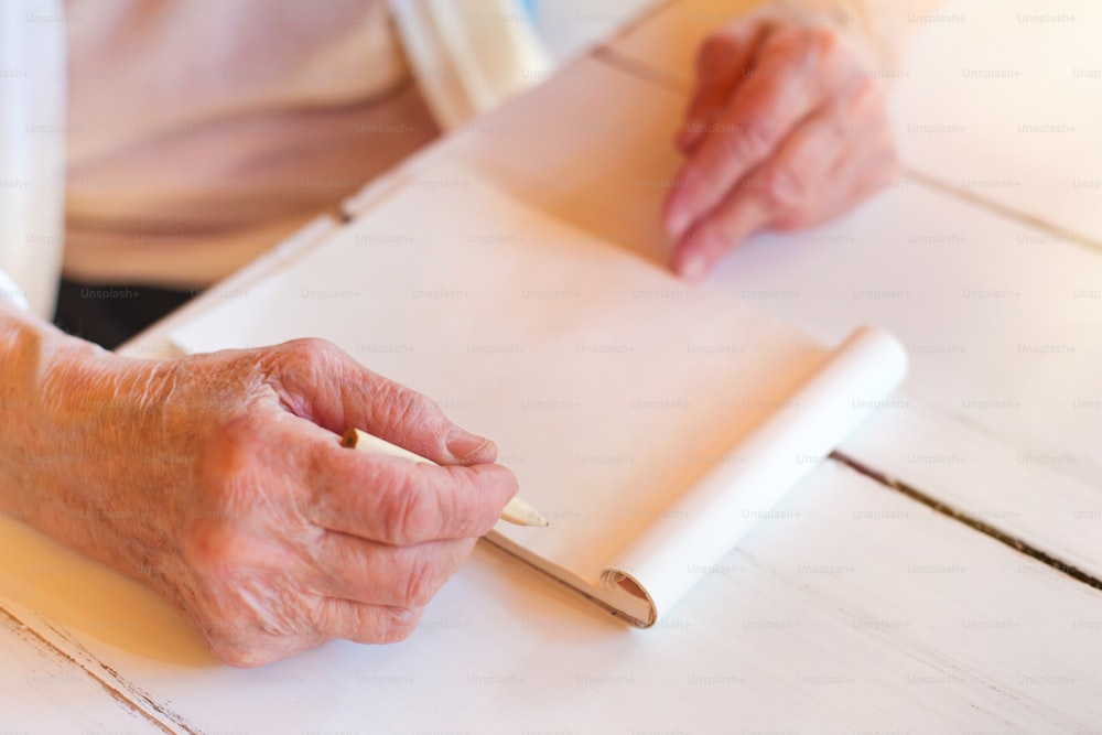 알아볼 수 없는 선배 여성의 손이 나무 흰색 책상에 글을 쓰고 있다.