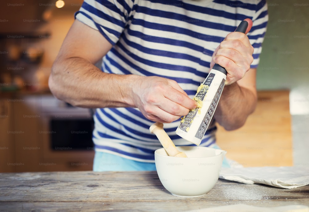 Man in the kitchen grating a piece of ginger